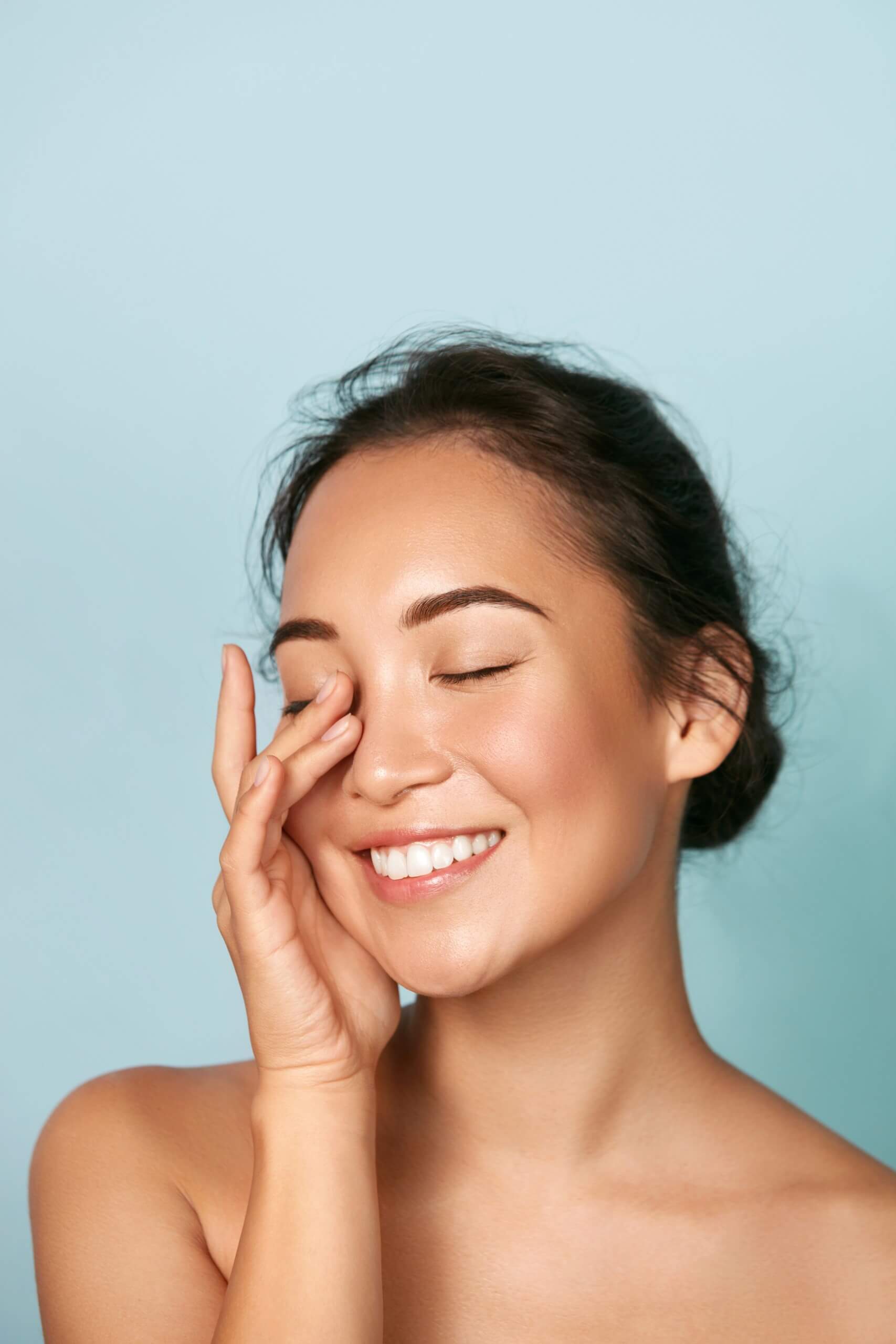A woman with a dark brown hair, glowing skin smiling joyfully, bluish background