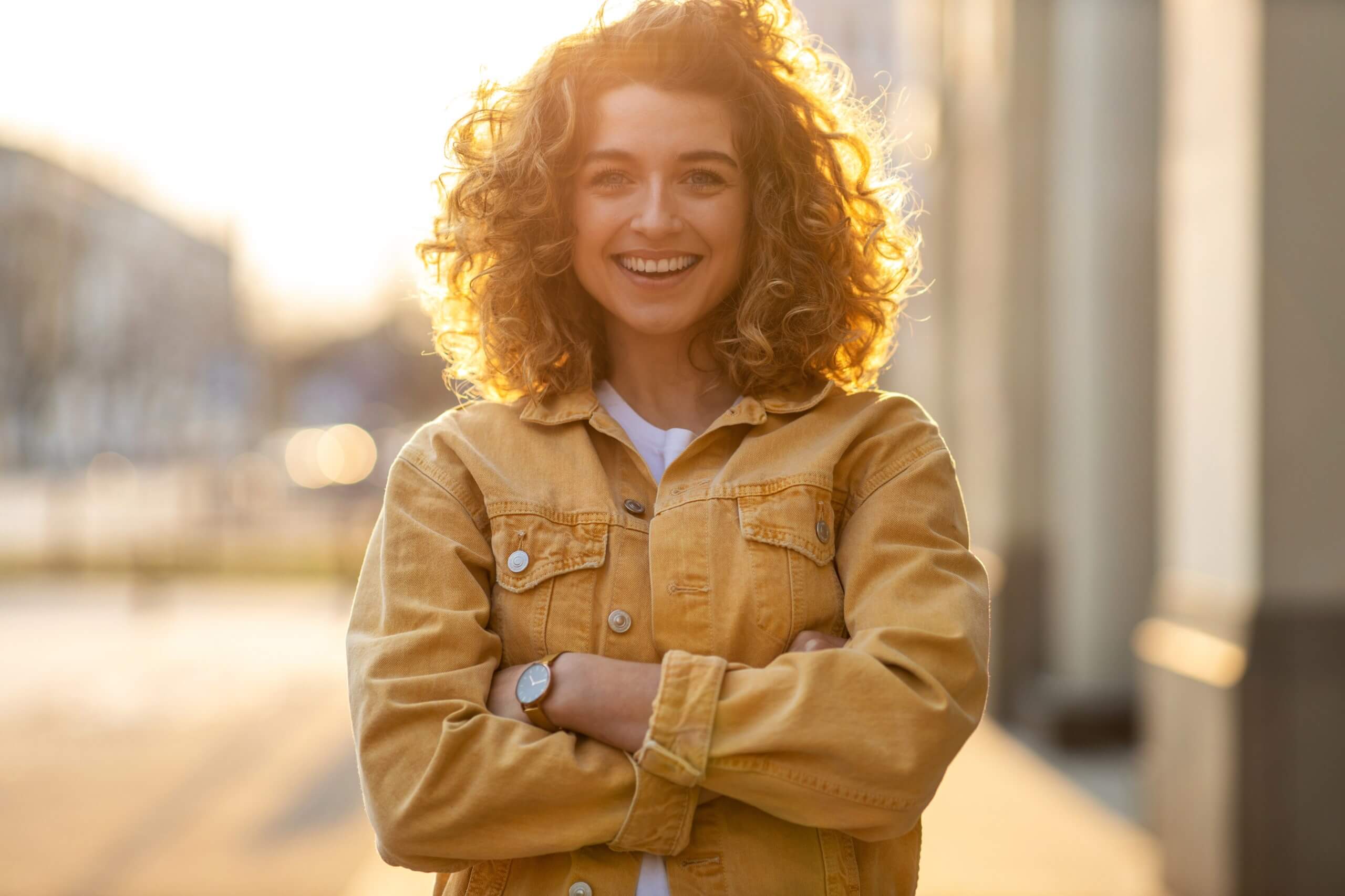 Smiling brunette woman on the street at sunset, the background is blurred.