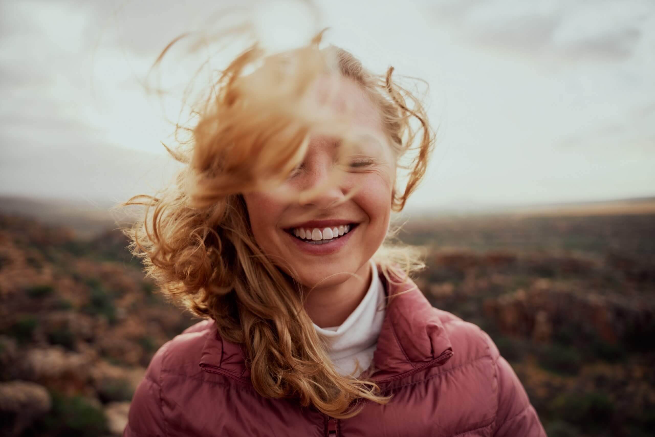Ginger woman smiling, wearing a jacket, standing outside on a overcast day