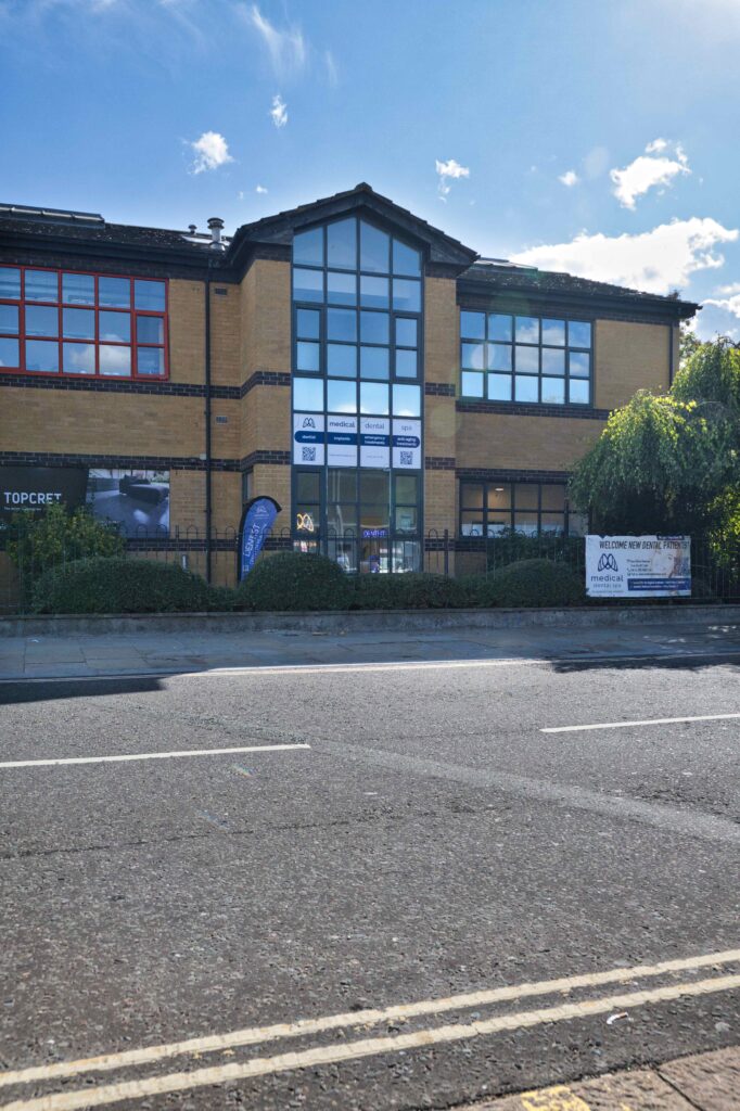 Modern two-story brick building with large glass windows, housing a medical, dental, and spa clinic, seen from across the street under a bright blue sky