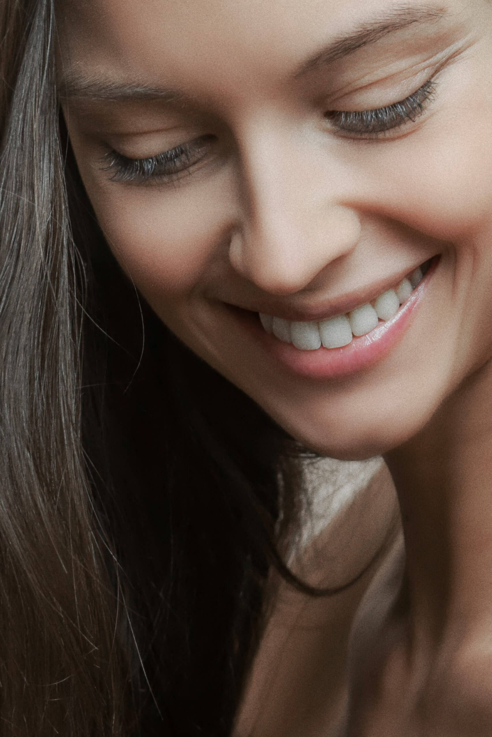 Close-up photo of a young woman with long eyelashes, brown hair, pink lips, smooth skin and white teeth, perfect nose