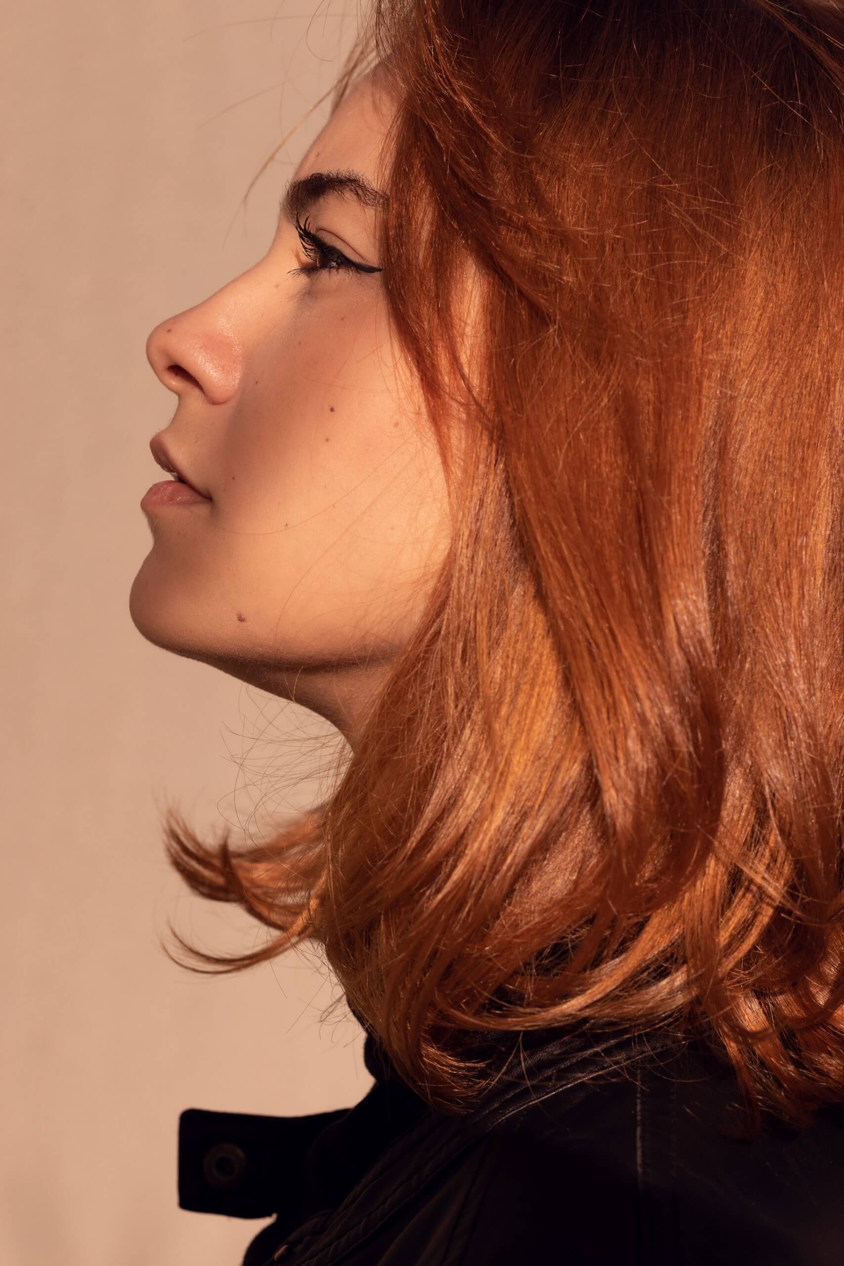 Close-up photo of a red hair woman, with brown eyes, pink lips and smooth skin.