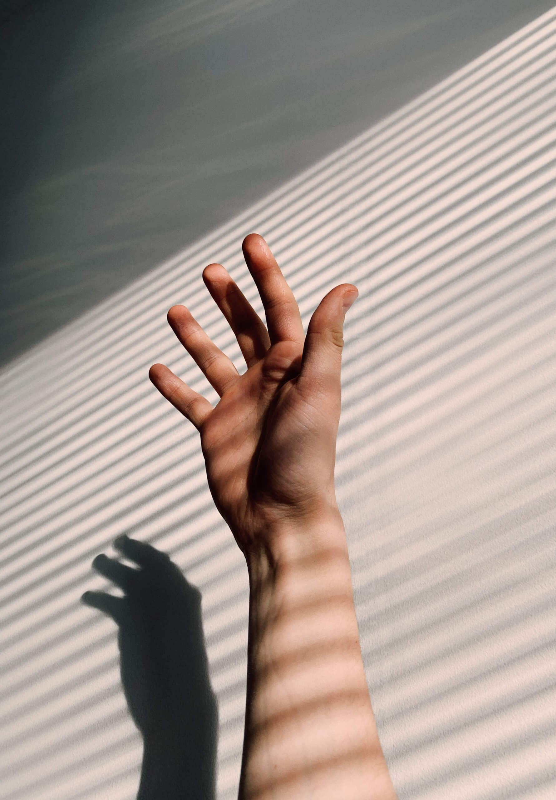 Hand and forearm close up photo. the hand pointing toward the wall at the background with shadows