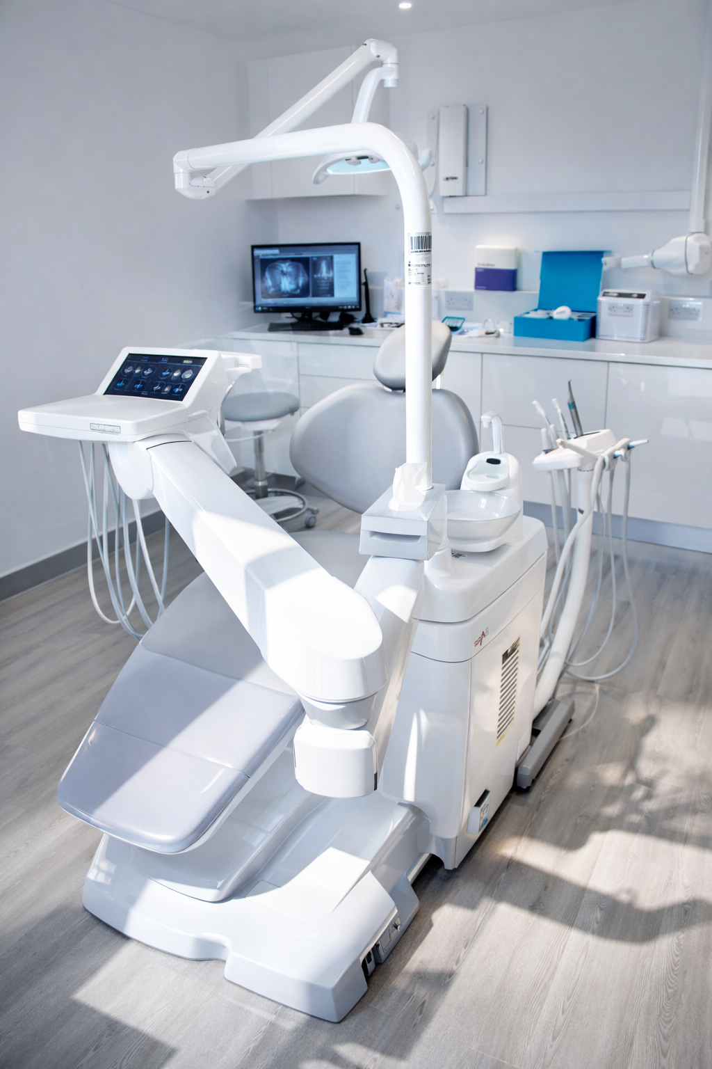 Bright, modern dental treatment room featuring a sleek, advanced dental chair with integrated touchscreen controls, overhead LED light, and professional instruments, set within a clean, minimalist clinic environment that conveys high-tech, contemporary dental care.